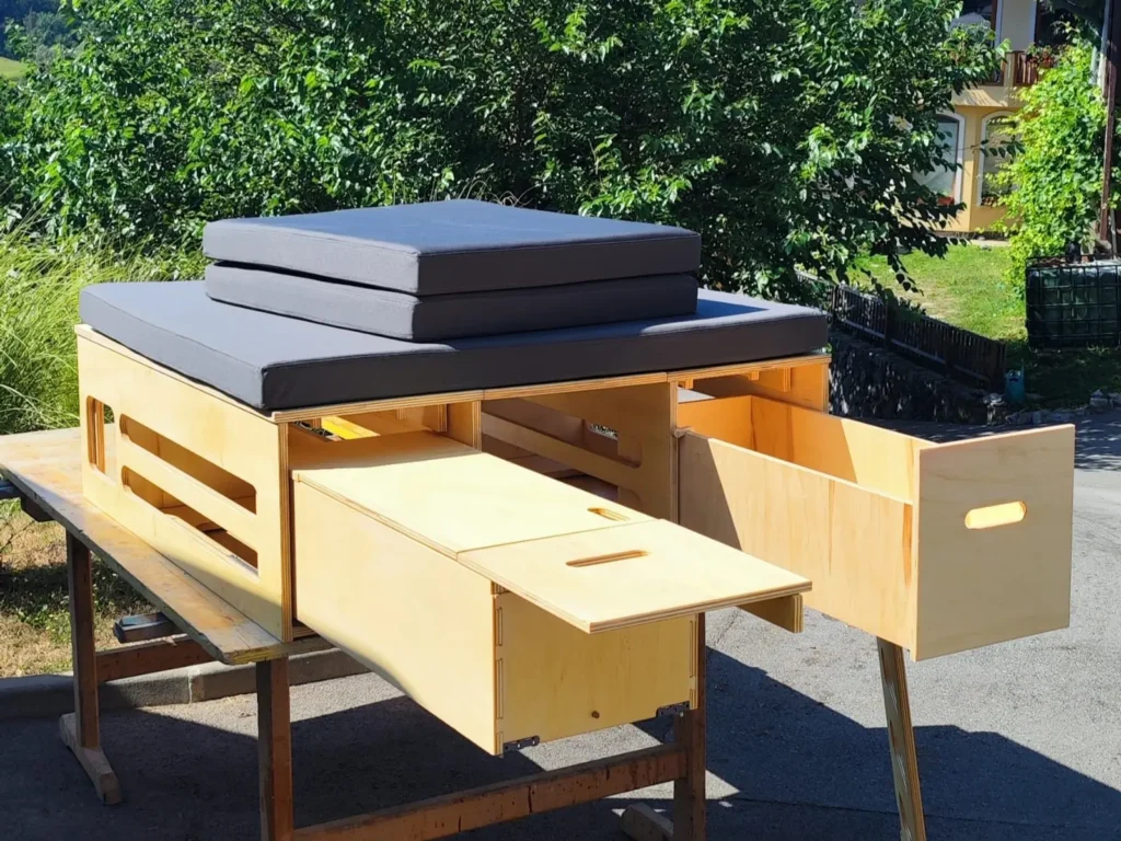 Kamping modul Vivabox z izvlečno kuhinjo, shranjevalnimi predali in spalnim ležiščem, postavljen zunaj kombija za prikaz funkcionalnosti